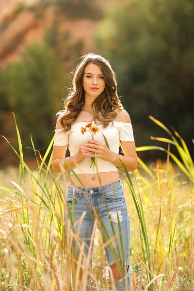 Sunset senior portrait of a girl holding flowers in a filed of tall grass by Amy K Photography