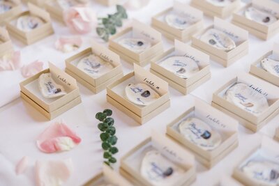 Wedding guest favors small boxes, each labeled with a name and soft greenery accents.