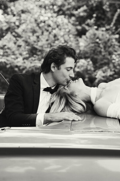 Timeless black and white photo of a bride and groom kissing on a vintage car—captured in Nashville, TN with a cinematic, editorial wedding style.