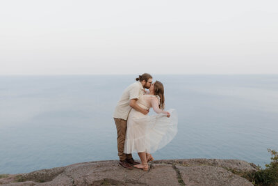 A person kissing their partner as they stand on an overlook looking out over water 