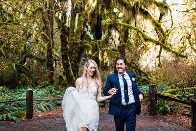 a couple running through the Hoh Rainforest in wedding attire after saying their vows during their Washington Elopement in Olympic National Park.