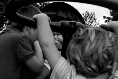 A dad swings his toddler daughter in his arms while she laughs and her baby sister looks on as mom is changing her. 