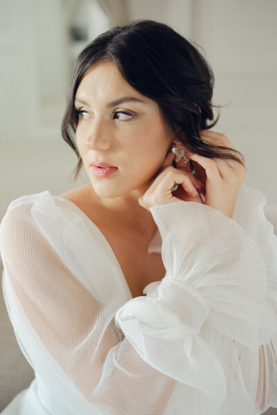brunette bride putting in a small pearl earring