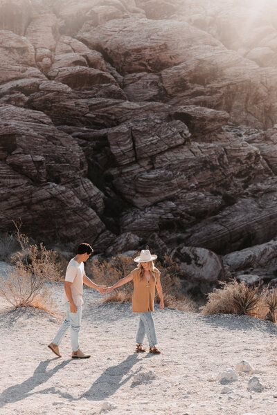 Couple walking in Arizona desert holding hands in front a rock mountainside