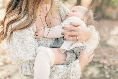 Close-up of a mother cradling her babygirl outdoors in a Kansas City park while wearing soft floral tones with natural light highlighting the bond between them