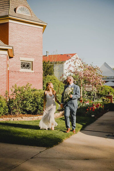 Couple walking hand-in-hand past a red brick building with garden views