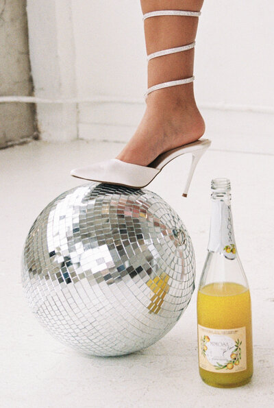 White heel sitting on a disco ball next to a bottle of mimosa