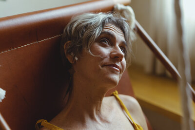 An older white woman looks up toward the ceiling, with a small smile. She has short gray hair and is wearing white earbuds.