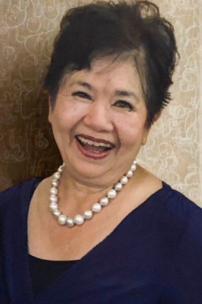 Author, speaker, and Christian life coach Nita Tin smiling warmly at the Scenic City Women’s Network event in Chattanooga, Tennessee. She is wearing a blue dress with pearls and standing in front of a taupe wallpaper wall with white decorative lines.