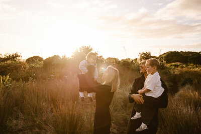 A mother holds her baby in the air during a family photoshoot with taranaki family photographer aimee kelly photography