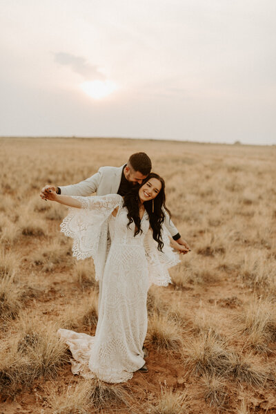 bride and groom spinning in grass field