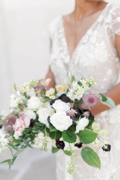 White, purple and green organic bouquet held by a bride