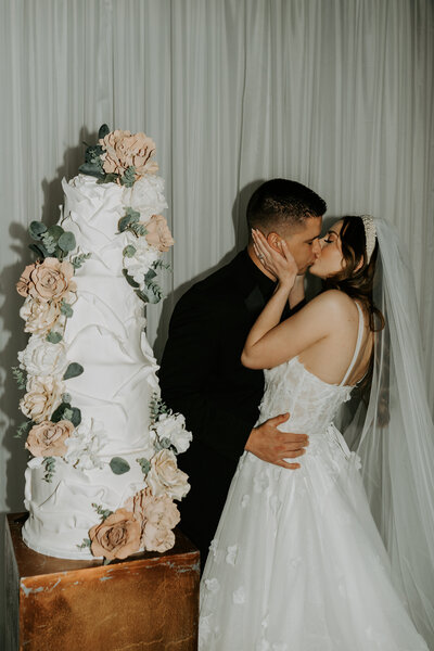 The Hudson St. Francis Bride & Groom kissing by cake, photographed by Wichita Wedding Photographer The Cantrells