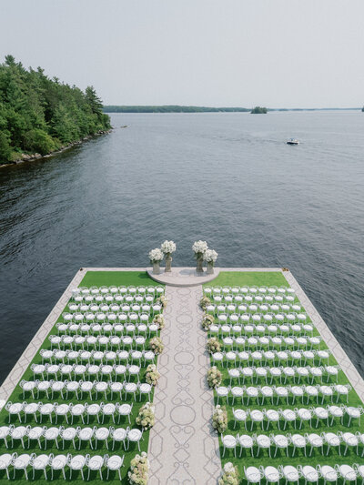 Wedding reception table, white table cloth, wooden cushioned chairs. Above the table are white bouquets and crystal chandeliers