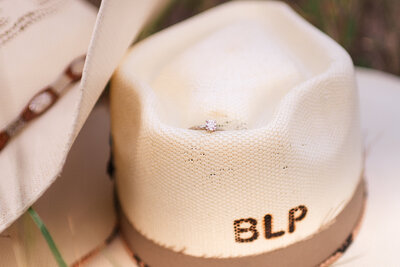 Close-up of monogrammed cowboy hat with engagement ring during engagement session in New Braunfels, TX.