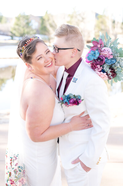 Bride kissing her bride while leaning in together and laughing and smiling at the camera