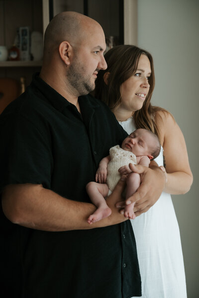 Mama en papa kijken naar buiten met hun pasgeboren baby in hun armen tijdens de newbornshoot.
