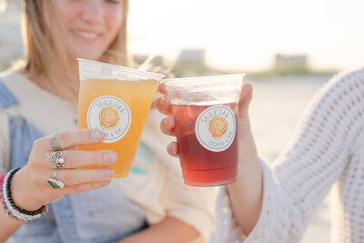 closeup of two baristas cheersing their sundial tea cups on the beach