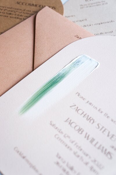 Painted wedding invitation with green and white paint and arched shape, sitting on wafer brown envelope