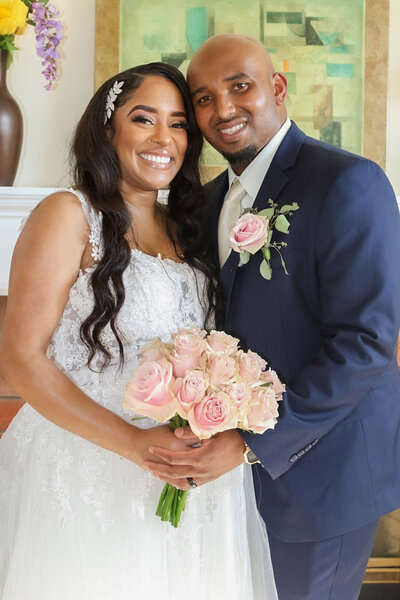 Smiling bride and groom holding a pink rose bouquet