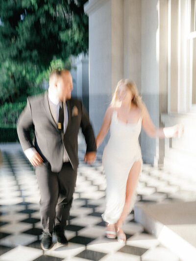 A engaged couple running through the halls of Sacramento Capitol buildling for a blurry modern photo holding hands in elegant modern attire.
