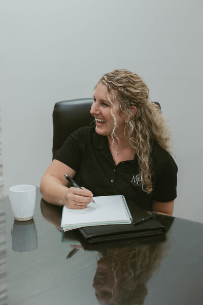 woman sitting at a table writing in a notebook while smiling