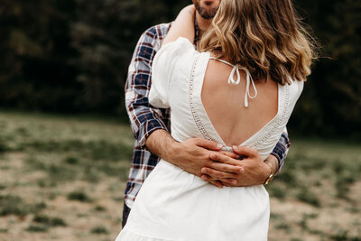 Close up photo of husband's hands wrapped around wife's waist. Photo captured at a park in the National Capital. Photography by Canberra-based wedding photographer, Acacia & Grace 