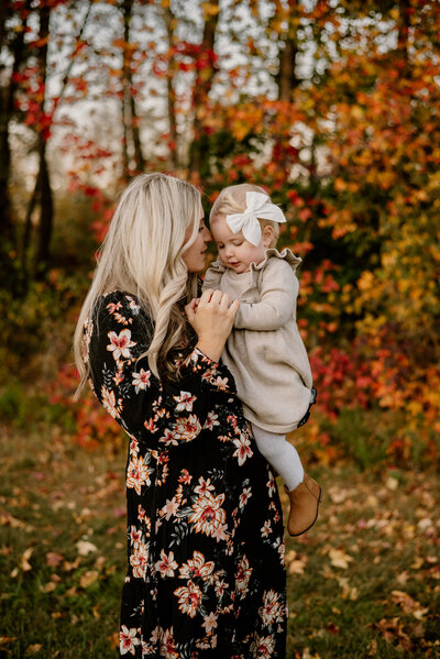 Mom in black floral dress holding baby girl while snuggling her cheek and holding her hands in Annapolis Maryland