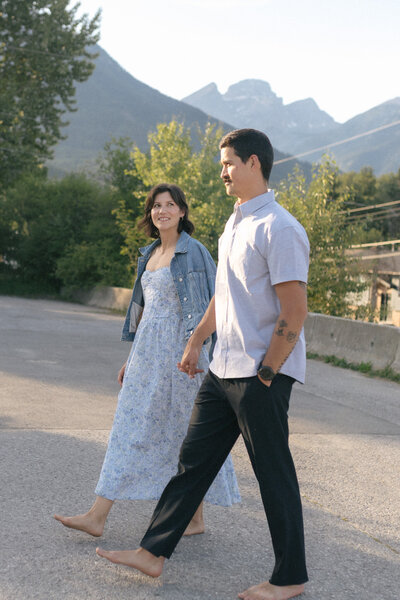 couple hold hands as they walk down the street with mountains in the background