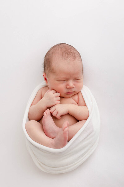 newborn baby wrapped in white with toes and hands showing. Sleeping on a white blanket during Portland Oregon newborn photography session.