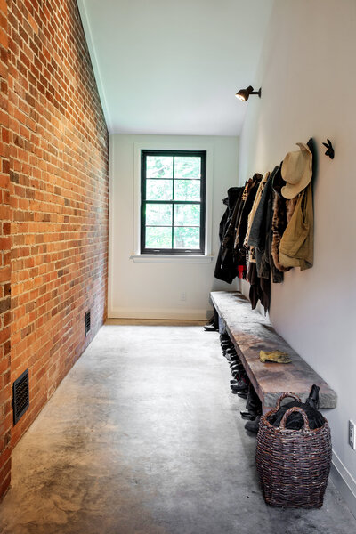 a hallway with coats hanging and boats under the bench.