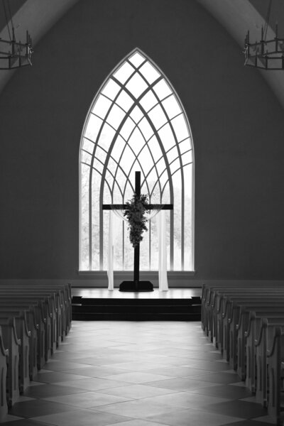 Black and white image of a cross decorated with florals in front of an arched window