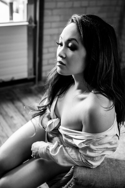 A black and white photo of a stunning woman with a button down shirt on, posing for boudoir photography in London, Ontario
