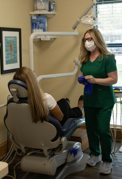 Patient in chair for routine checkup while the hygienist is prepping station for cleaning.