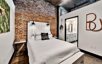 Bedroom with Queen bed and bathroom access in this three-bedroom, two-bathroom industrial modern loft condo in the historic Behrens building in downtown Waco, TX.
