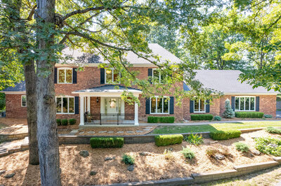 Photo of the front of a large brick house set into trees.