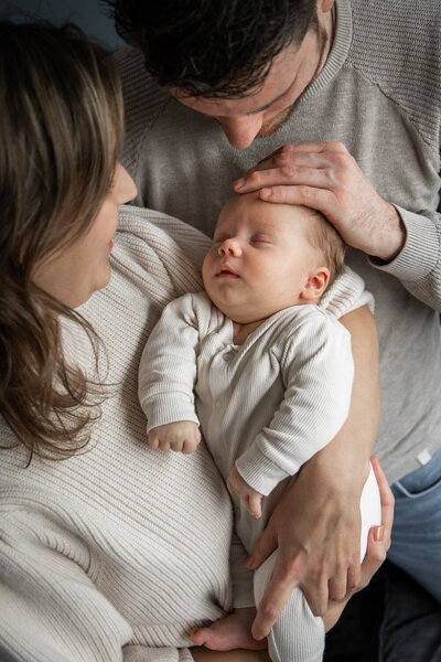 Vader en moeder knuffelen met hun baby tijdens een ontspannen newbornshoot thuis