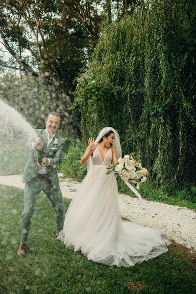 Groom spraying bottle of champagne as celebration in a garden while bride watches, used as a call to book a mentorship call.