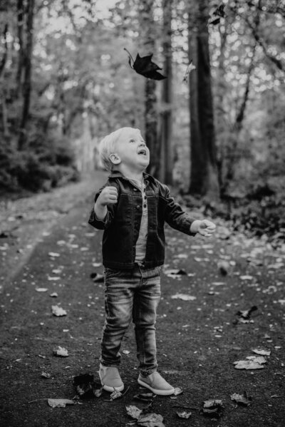 Black and white photo of toddler boy looking at leaves he threw in the air at Patapsco State Park in Maryland