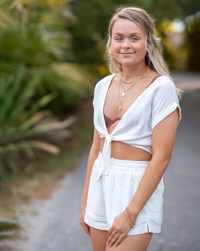 senior girl wearing white outfit with palm trees in background
