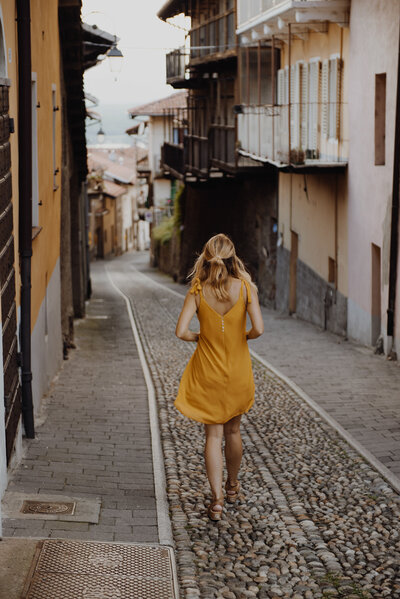 Woman in a yellow dress walking through a cobblestone alley, symbolizing the journey to clarity and balance.