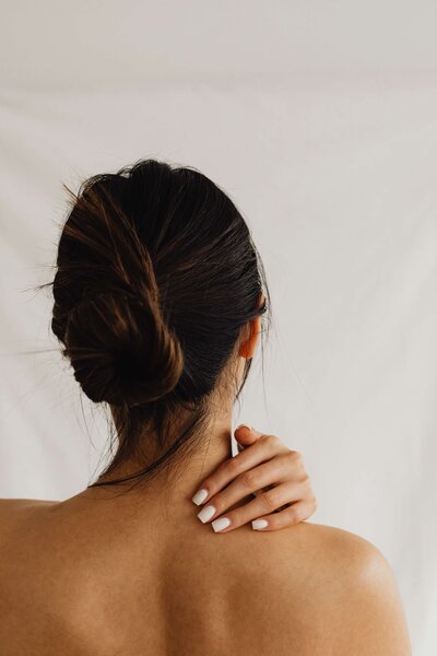 The back of a women with her hair pulled. up and hand touching her back.