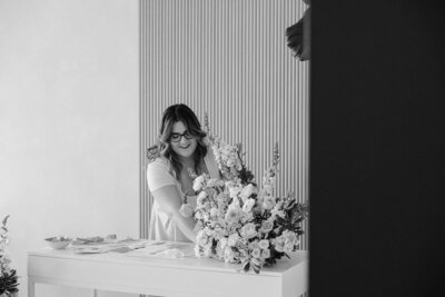 Black and white photo of wedding planner, Zelie & Co., fixing a floral arrangement on a table