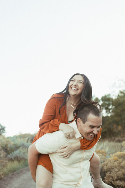 Husband giving wife a piggy back ride and both laughing.