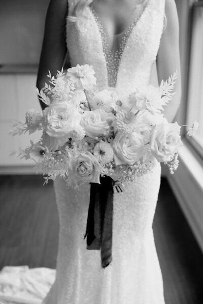 Close-up of a bride holding her all-white floral bouquet with black ribbon, showcasing modern elegance. Perfect for couples seeking wedding florals in Ottawa.
