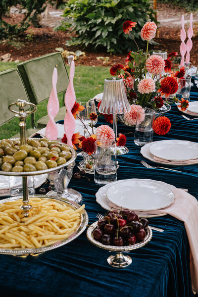 A bride stands behind a table with a large floral arrangement, representing wedding management offerings by Birdie June Events and Rentals. 