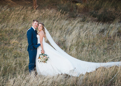 Groom in navy suit holds his bride in his arms while wind blows her long veil behind her