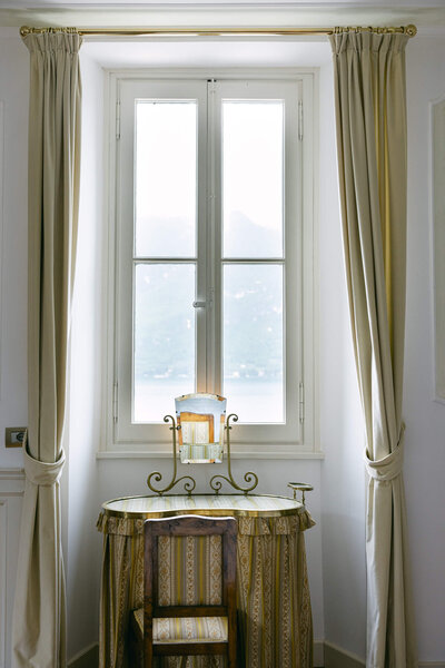 A photo of a desk and table by the window in a bedroom in villa aura del lago with a view of lake como in Italy