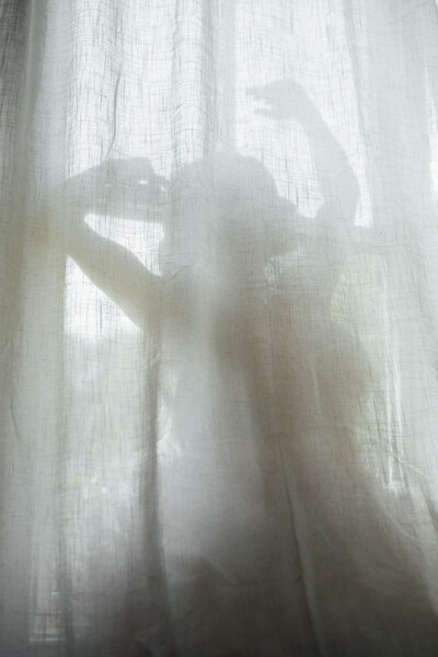 Silhouette of a bride behind sheer curtains