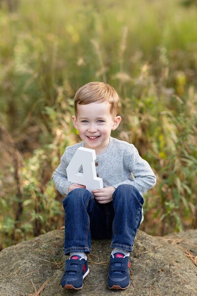 Little boy sitting down smiling holding number 4